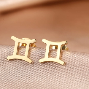 Macro view of gold stainless steel Gemini zodiac earrings on a silk fabric background