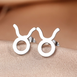 Macro shot of silver Taurus zodiac stud earrings on silk fabric with mirror polish