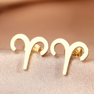 Macro shot of gold Aries zodiac sign stud earrings on elegant silk background