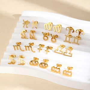 Collection of 12 gold stainless steel zodiac earrings displayed on a white textured stand