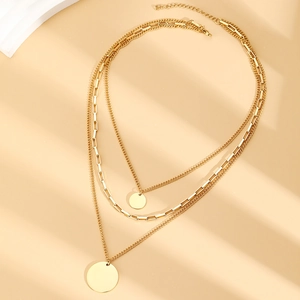 Detailed view of triple-layered gold necklaces with round pendants on minimalist background