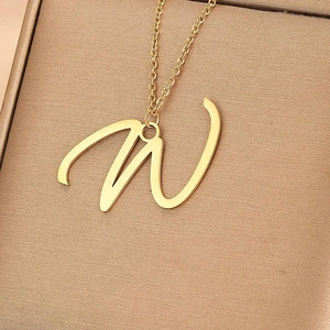 Vue macro d'un collier avec pendentif lettre W dorée cursive dans un écrin à bijoux texturé