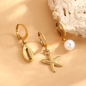 Detailed close-up of gold starfish, shell, and pearl charm earrings on a sandy background