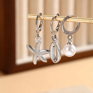 Detailed macro view of starfish, seashell, and pearl charms on silver earrings