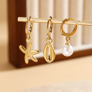 Macro shot of gold starfish, shell, and pearl drop earrings in a 3-piece nautical set