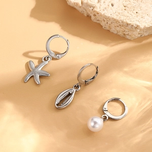 Detailed set of three silver starfish shell and pearl drop earrings on sandy background