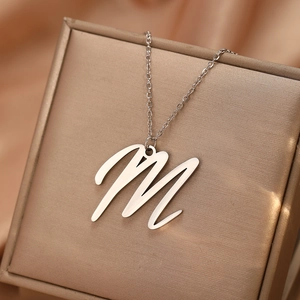 Vue macro du pendentif lettre M en métal brossé argenté sur une chaîne délicate