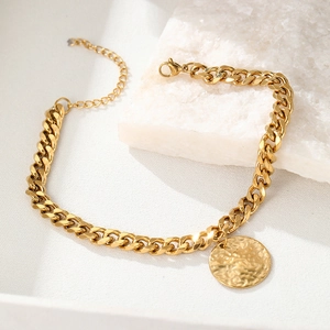 Detail of gold curb chain anklet featuring a textured round pendant and lobster clasp