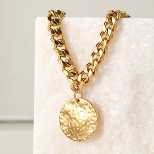 Close-up of gold Cuban chain anklet featuring a textured round hammered metal disc pendant