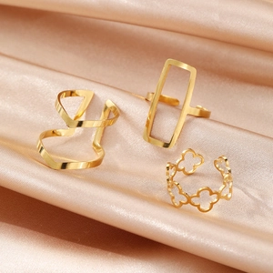 Detailed close-up of three gold adjustable geometric and clover rings on silk fabric