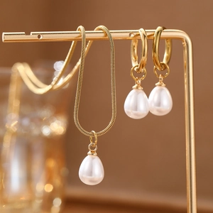 Close-up of gold snake chain necklace and drop pearl earrings on a display stand