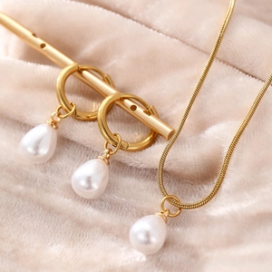 Close-up of golden necklace and teardrop pearl earrings on soft fabric display