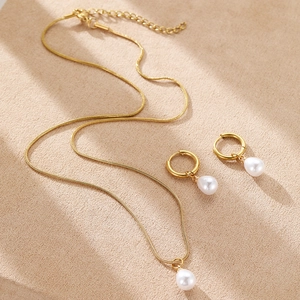 Detail of gold snake chain necklace and drop pearl earrings on textured fabric