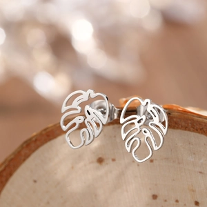 Gros plan de boucles d'oreilles feuilles de monstera creuses en argent sur bois
