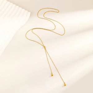 Detail of 18K gold-plated Y-shaped necklace with elegant tassel beads on beige background