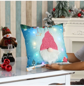 Close-up of LED glowing Christmas gnome pillow cover with plush beard and snowy house pattern