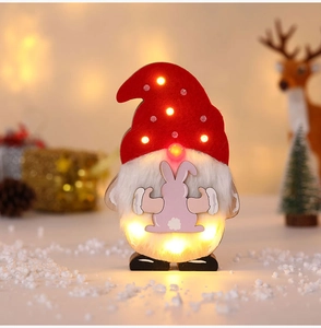 Nahaufnahme eines beleuchteten Weihnachtswichtels mit LED-Mütze auf einem Holzsockel