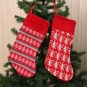 Red knitted Christmas stocking set with pine tree patterns hanging on a festive tree