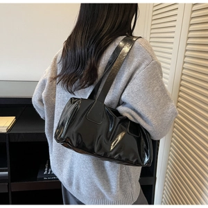 Detail of minimalist black patent leather baguette bag with padded texture and wide strap