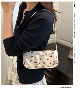 Detail view of white underarm bag with red cherry prints and golden metal zipper