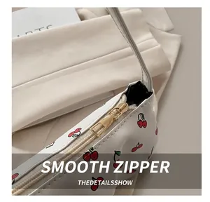 Detail view of smooth golden metal zipper on a white cherry print shoulder bag for women