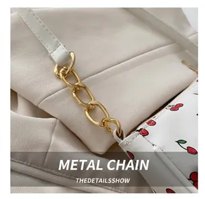 Detail of white litchi grain leather bag with cherry print and gold chain links
