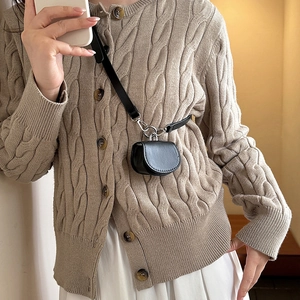 Mini sac bandoulière noir en cuir avec boucles argentées porté sur un cardigan beige