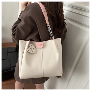 Detail of beige tote bag with pink straps and a cute white cat bag charm accessory
