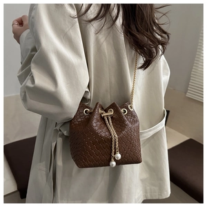 Detail of dark brown woven bucket bag featuring gold chain and elegant pearl drawstrings
