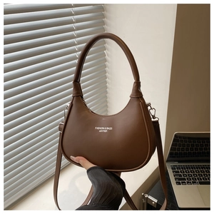 Detail of a brown leather crescent handbag featuring minimalist white logo lettering