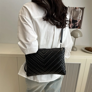 Minimalist black V-quilted crossbody bag with metallic studs on a stylish model