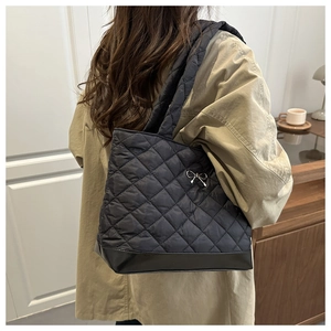 Close-up of black quilted tote bag with silver bow detail in a cozy lifestyle setting