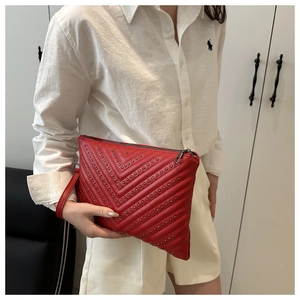 Detail of red quilted leather clutch featuring elegant metal studs and wristlet strap