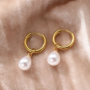 Close-up of gold hoop earrings with white teardrop pearls on a soft champagne velvet cloth