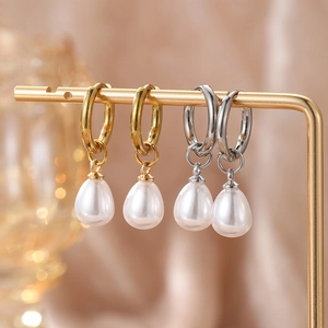 Elegant gold and silver hoop earrings featuring drop-shaped pearls on a minimalist display