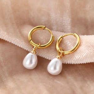 Elegant gold hoop earrings with white teardrop pearls on soft champagne fabric