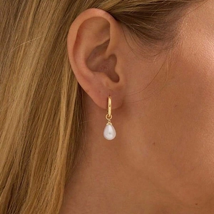 Detailed close-up of a drop-shaped pearl earring with a golden hoop on a model