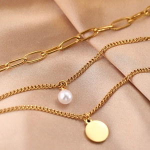 Detail of layered gold necklace with white pearl and round metal pendant on satin
