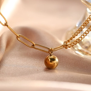Détail du pendentif boule dorée polie sur chaîne trombone et tissu satiné