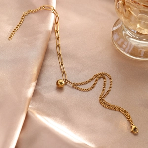 Détail d'une chevillère en acier doré avec pendentif boule sur un tissu en soie champagne