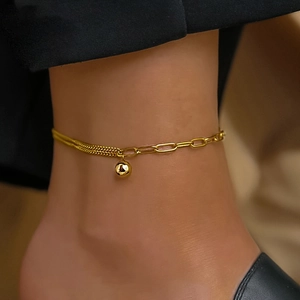 Détail d'une chevillère dorée avec des chaînes asymétriques et un pendentif perle polie