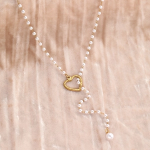 Gros plan sur pendentif cœur évidé et collier de perles au fini doré élégant