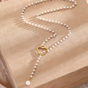 Détail macro du pendentif cœur doré et collier perles sur une boîte à bijoux beige