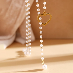 Vue macro du pendentif cœur doré et des perles lustrées sur un collier en forme de Y