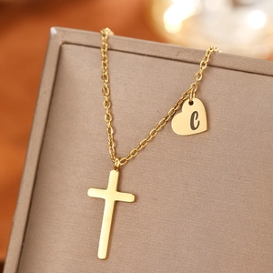 Detail of gold cross and letter C heart pendant on a minimalist stainless steel chain