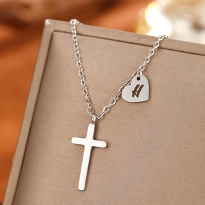 Macro shot of silver stainless steel cross and heart pendant with H initial engraving