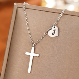 Macro shot of silver cross and heart charm with J engraving on a premium jewelry box