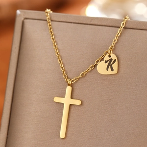 Detail of gold stainless steel necklace with cross and heart charm engraved with letter K