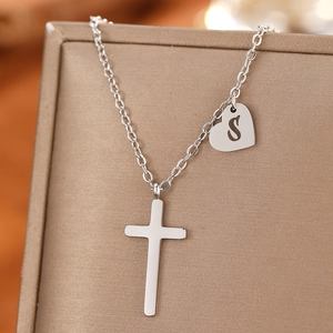 Macro shot of silver stainless steel cross and heart pendant with letter S engraving