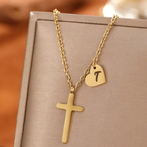 Detail of gold necklace featuring a sleek cross and heart pendant with letter T engraving